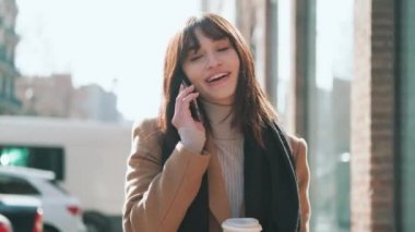 Şehrin sokaklarında yürürken bir fincan kahve içerken cep telefonuyla konuşan güzel bir genç kadının videosu..