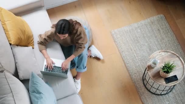 在家里客厅的地板上 一个漂亮的年轻女人坐在沙发上用笔记本电脑工作的视频 — 图库视频影像