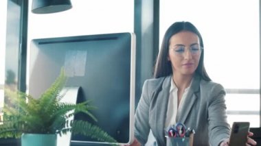 Ofiste bilgisayarla çalışırken cep telefonunu kullanan güzel bir iş kadınının videosu..