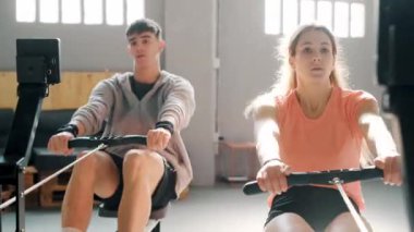 Spor salonunda kürek çekme makinesiyle çalışan atletik kadın ve adamın videosu..
