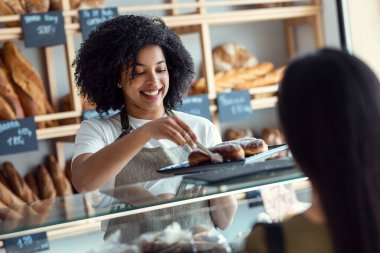 Shot of smiling woman seller giving fresh biscuits to cheerful woman in the pastry shop.