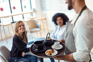 Pastanede gülümseyen kadınlar için kahve ve pasta servisi yapan yakışıklı garson..