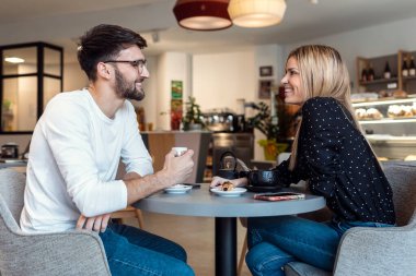 Shot of young lovely couple talking and laughing while drinking coffee together in pastry shop.