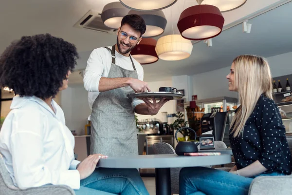 빵집에서 테이블에서 미소짓는 여자들을 커피와 과자를 제공하는 잘생긴 웨이트리스 남자의 — 스톡 사진