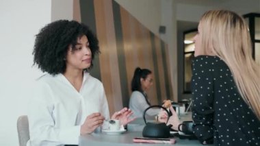 Video of young happy women talking and laughing while drinking coffee together in pastry shop.