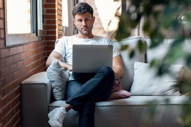Shot of smart man working with her laptop while sitting on a couch at home