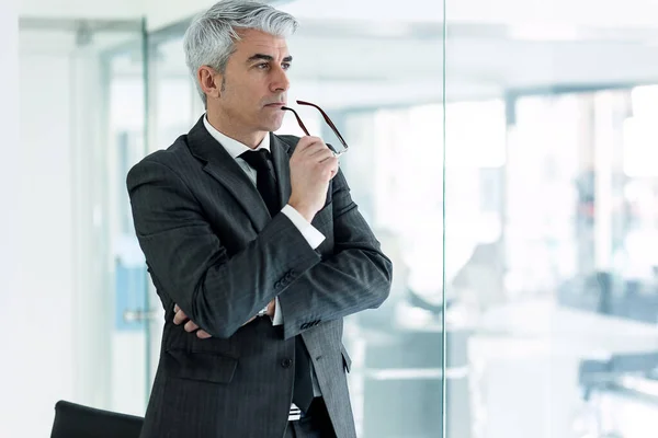 Shot of mature concentrated businessman thinking while looking forward standing next to the window in a modern startup.