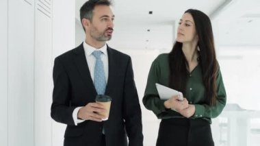 Modern bir girişimde konuşurken ve yürürken dijital tabletle çalışan iki çekici iş adamının videosu.