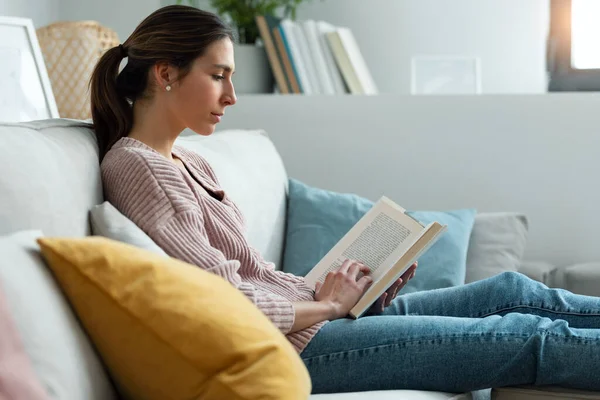 Skjuten Söt Ung Kvinna Läser Bok När Sitter Soffan Hemma — Stockfoto