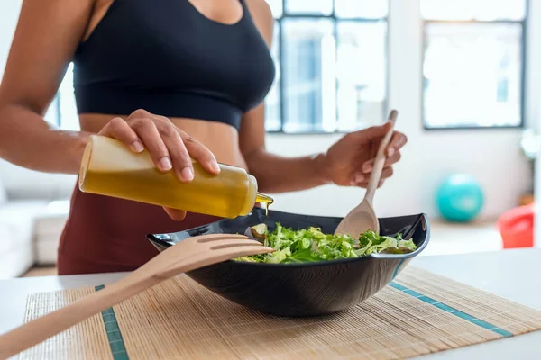 Close up of sporty woman seasoning the salad with oil in the kitchen at home.