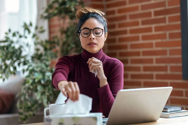 Hasta kadının evdeki oturma odasında dizüstü bilgisayarla çalışırken mendile hapşırması..