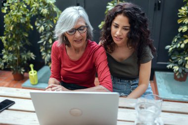 Moda büyükannesi ve güzel torununun bahçede bir bankta dizüstü bilgisayar kullanırken konuştuğu bir fotoğraf..