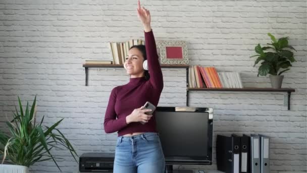 自宅のリビングルームで踊りながら携帯電話で音楽を聴いているかなり若い女性のビデオ — ストック動画