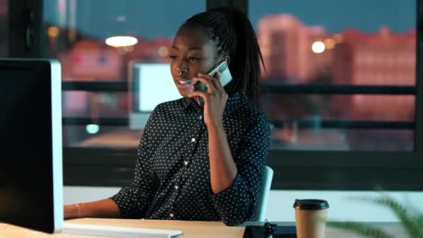オフィスでノートパソコンを操作しながら携帯電話で話す自信に満ちた若いビジネス女性のビデオ — ストック動画