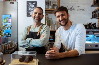 Portrait of two handsome owners selling fresh pastry and loaves un bread section and smiling at healthy pastry shop.