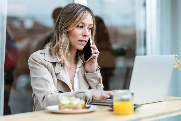 Shot of pretty blonde woman talking with smartphone while having breakfast sitting in the eco bar terrace.