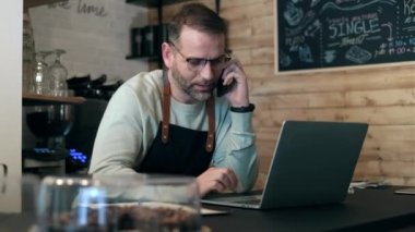 Video of handsome mature owner bakery working while analyzing report for order delivery with laptop in a pastry shop.