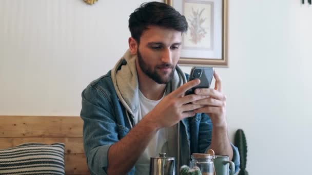 Vídeo Jovem Bonito Usando Seu Smartphone Enquanto Bebe Uma Xícara — Vídeo de Stock