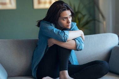 Shot of depressed woman sitting on the coach at home