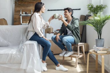 Genç ve güzel bir çiftin bir fincan kahve içerken yeni evlerinde karton kutuların etrafında rahatlarken çekilmiş fotoğrafları.