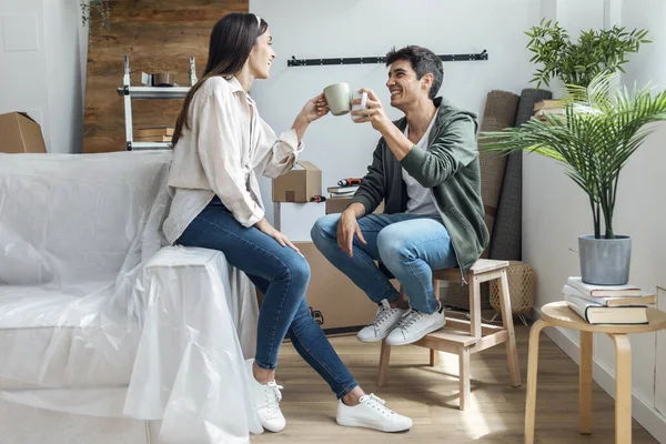 Genç ve güzel bir çiftin bir fincan kahve içerken yeni evlerinde karton kutuların etrafında rahatlarken çekilmiş fotoğrafları.
