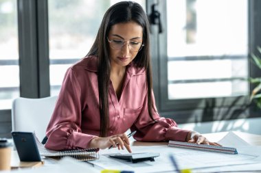 Shot of concentrated young business woman working with blueprint in the office.