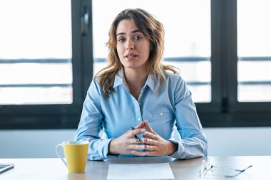 Shot of confident business woman doing video call while looking at camera in modern startup office.