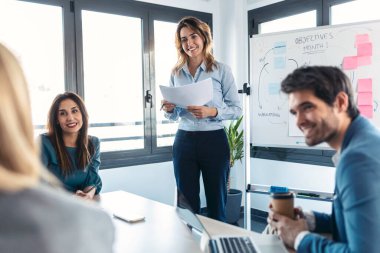 Shot of elegant businesswoman having a meeting front of white blackboard and explain a project to her colleagues on coworking place.
