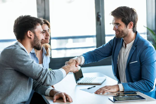 Shot Van Aantrekkelijke Makelaar Schudden Handen Met Jong Stel Ondertekening — Stockfoto