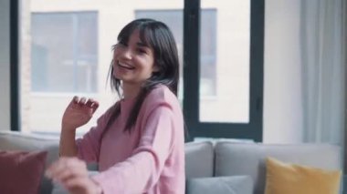 Video of pretty young woman listening to music while dancing in the living room at home.