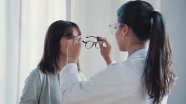 Video of  female doctor choosing while proving eyeglasses to mature beautiful patient in medical consultation.