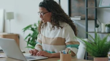 Video of concentrated beautiful business woman working with laptop in living room at home.