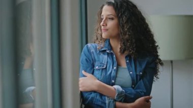 Video of beautiful young woman thinking while looking forward standing next to the window at home.