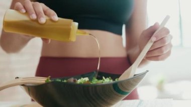 Video of close up of beautiful young woman making a healthy salad while singing and listening music with headphones in the kitchen at home.