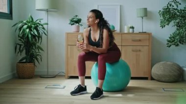 Video of sporty young woman drinking detox juice while doing exercise with the ball at home.