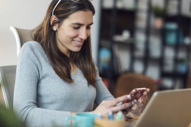 Shot of smart business woman using mobile phone while working with laptop in living room at home.