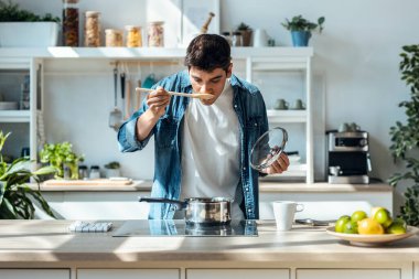 Shot of handsome mature man tasting the food he is preparing in the kitchen at home.