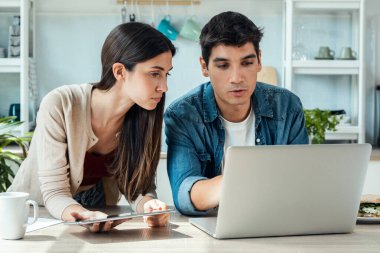 Shot of beautiful lovely couple using their laptop and digital tablet to searching voyage in the kitchen at home.