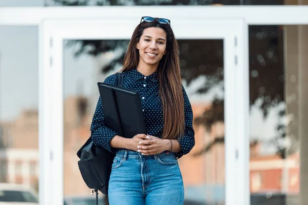 Shot of executive woman laughing at camera outdoors while holding a folder on street.