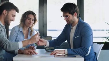Ofisteki evi almak için çiftle konuşurken elektronik tablette ev planlarını gösteren yakışıklı bir emlakçının videosu..