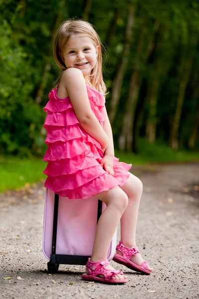 Маленькая девочка сидит на своем чемодане — стоковое фото