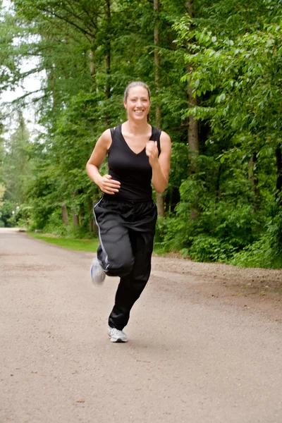 Mujer joven y deportiva corriendo por un camino de bosque —  Fotos de Stock