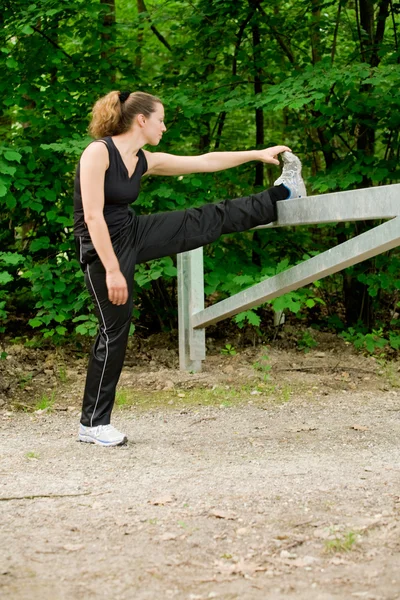 Joven mujer adulta estirando su pierna en un camino de bosque —  Fotos de Stock