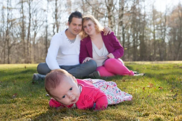 Baby girl in the grass parents on the background — Stock Photo, Image