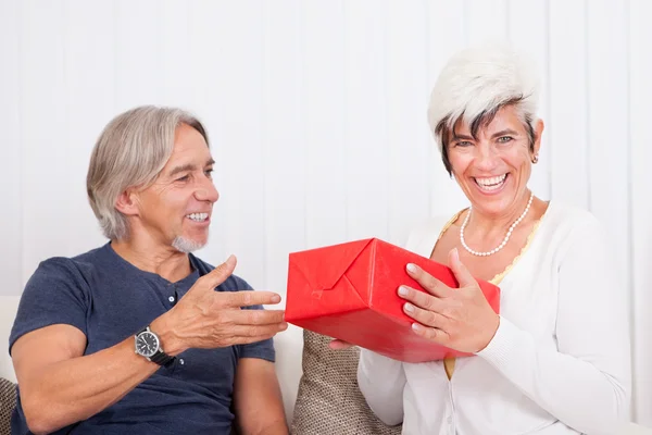 Rindo casal sênior com caixa de presente vermelho — Fotografia de Stock