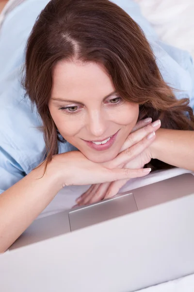 Vrouw ontspannen op haar bed met laptop — Stockfoto