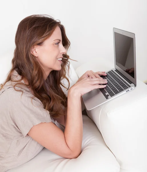 Mulher relaxante no sofá usando laptop — Fotografia de Stock