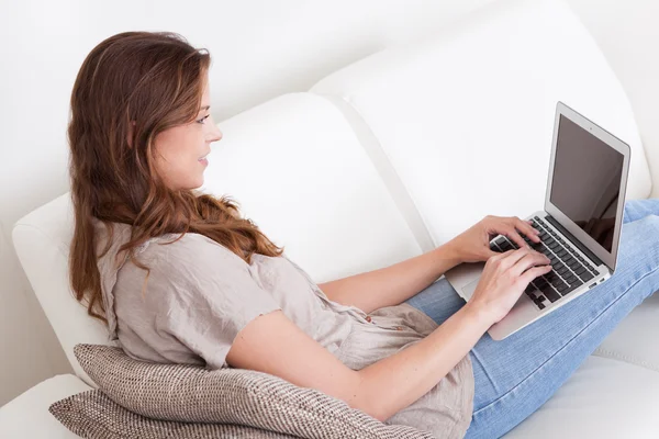 Mujer relajante en el sofá utilizando el ordenador portátil — Foto de Stock