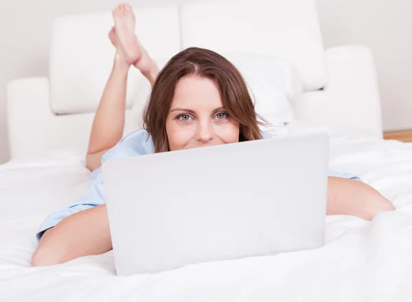 Woman relaxing on her bed with laptop — Stock Photo, Image