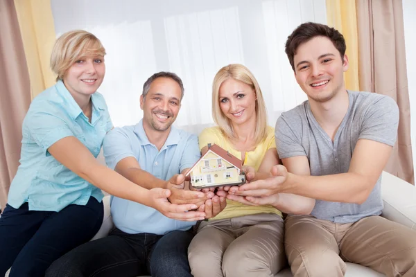 Família feliz segurando uma casa modelo — Fotografia de Stock